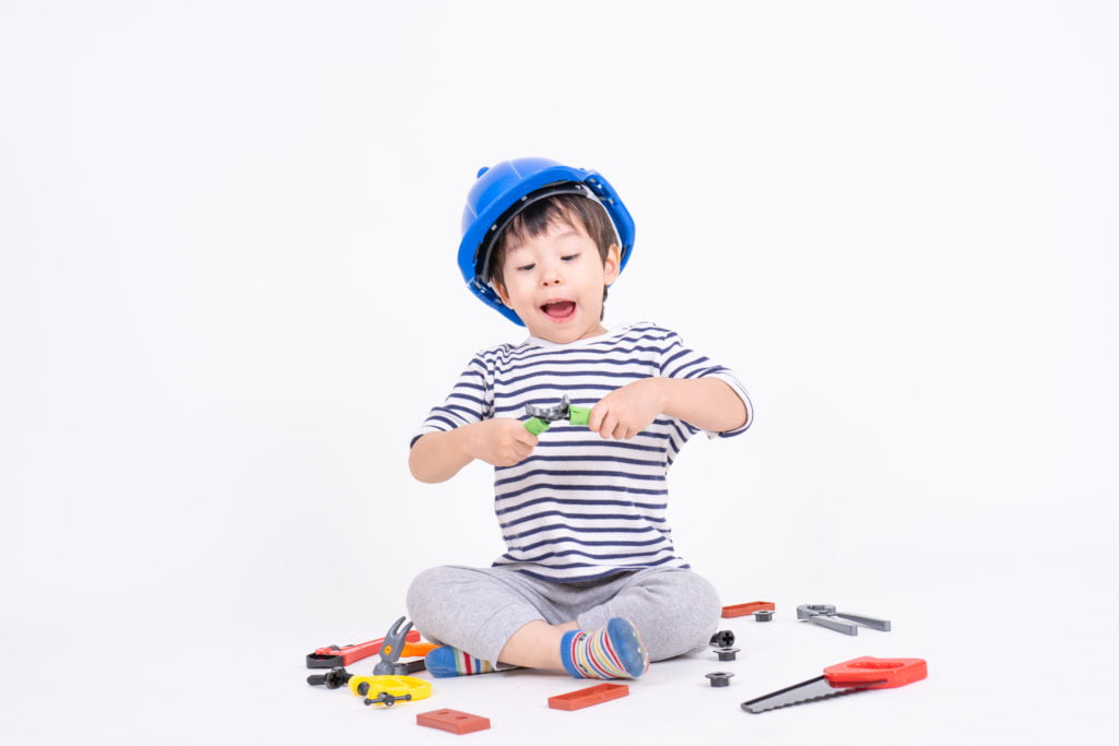 little boy wearing blue helmet sitting playing with construction equipment toy white